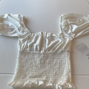 Vit blus från Chiara Forthi - Säljer en vit blus med puffärmar, knappar, en tajtare underdel och en guld bricka på baksidan. Blusen är helt ny, med prislapp och är i storlek S