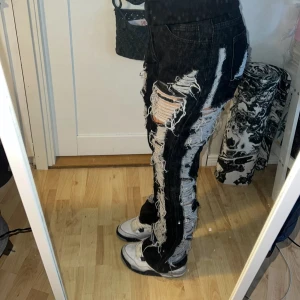Svarta jeans flared- streatwear style  - Svarta jeans med slitna detaljer och hål längs hela benen. Byxorna har en rak passform och utsvängt längst ner. De är lite imellan low-mid Rise
