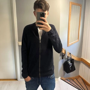 Svart zip-jacka  - Säljer en svart zip-jacka från H&M i storlek M. Jackan har en enkel design med dragkedja framtill och ribbad krage. Perfekt för lager-på-lager och passar till det mesta. Klassisk och stilren modell.