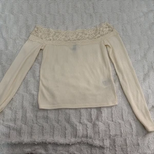 Offshoulder ribbad topp med spets - Säljer en krämvit offshoulder topp med ribbad struktur och bred spetskant upptill. Långärmad och superfin till både jeans och kjol. Perfekt för dig som gillar romantisk stil!