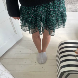 Grön blommig volangkjol från Neo Noir - Supersöt kortkjol från Neo Noir i grönt med blommigt mönster och volanger. Kjolen har smock i midjan och är tillverkad i lätt och luftig polyester med viskosfoder. Perfekt för dig som gillar färg och mönster!