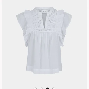 Vit blus med volang från Neo Noir - Säljer en luftig vit blus från Neo Noir med v-ringning, volangdetaljer och korta ärmar. Blusen har fina spetsinslag och ett romantiskt uttryck. Perfekt för vår och sommar! Endast använd en gång☺️