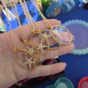 Guldiga halsband med sjöstjärna - Unika halsband med oval guldfärgad kedja och hänge, där en liten sjöstjärna är innesluten i transparent resin. Perfekt för dig som älskar havet och vill ha en cool detalj till din outfit. Hängena är tunna och glansiga, med en riktigt somrig vibe.  Handgjorda med kärlek, skriv vilken du vill ha vid köp.
