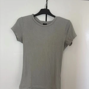 Grå basic t-shirt från Gina Tricot - En enkel grå t-shirt från Gina Tricot i storlek S. Modellen är klassisk med rund hals och korta ärmar, perfekt för en chill och clean look. Materialet är mjukt och känns skönt mot huden, t-shirten har en normal passform och passar till allt.