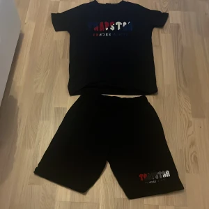 Svart t-shirt från Trapstar - Svart t-shirt med tryck i rött, blått och vitt framtill från Trapstar. Klassisk rund hals och korta ärmar, perfekt för chill dagar. Materialet känns mjukt och skönt mot huden. Snygg och enkel design med färgglad logga.