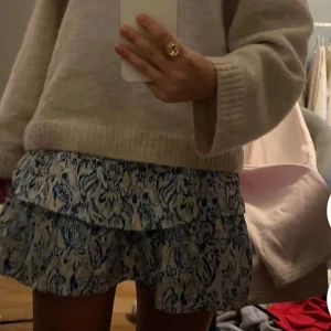 Blåvit volangkjol med mönster - Skriv om ni vill ha mer bilder.Supersöt kort kjol med blått och vitt mönster, bred smock i midjan och dubbla volanger. Perfekt för dig som gillar en luftig och somrig stil. Kjolen har en lätt och flowy känsla och passar perfekt till sneakers eller sandaler.