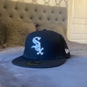 Svart White Sox keps från New Era, profil för mer - Säljer en svart New Era 59FIFTY keps med White Sox-logga i vitt framtill och MLB-logga baktill. Klassisk flat brim och broderade detaljer. Perfekt för dig som gillar sportig streetstyle och vill ha en snygg accessoar med baseball-vibe.