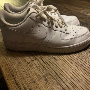 Nike Air Force 1  - Säljer ett par klassiska Nike Air Force 1 sneakers i helvitt skinn med rund tå och platt sula. Skorna har snörning och perforerade detaljer på tån för extra ventilation. Perfekt för dig som gillar clean och tidlös streetstil. De är i nyttskick. Storlek 44.5