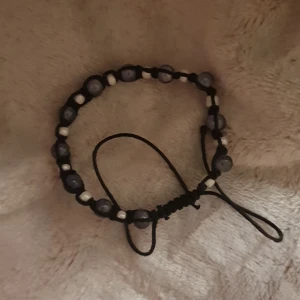 Svart och vit pärlarmband med snörning - Snyggt handgjort armband med svarta snören och pärlor i mörkgrått och vitt. Armbandet har justerbar snörning så det passar de flesta handleder. Perfekt för dig som gillar en enkel men cool stil med pärldetaljer.