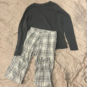 Pyjamas från Cubus i XS - Säljer ett par vita croppade byxor från Cubus i storlek XS. Byxorna har ett grått rutmönster och är tillverkade i mjukt bomullsmaterial. De har resår i midjan och en praktisk ficka på sidan. En grå tröja som är slapp, perfekt för chill dagar eller häng med kompisar.