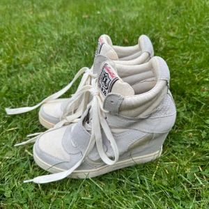 Vita wedge sneakers med snörning - Snygga vita wedge sneakers med högt skaft och snörning, samt kardborreband över foten. Skorna har en blandning av mocka och textilmaterial, med en plattformsklack som ger extra höjd. Märke med  text på plösen. Perfekt för dig som gillar Isabel Marant sneakers. Lite småfläckar.