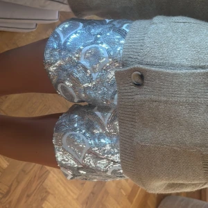 Silvriga paljettshorts med mönster - Glittriga shorts i silver med paljetter och ett unikt, böljande mönster i vitt. De har en loose passform och är perfekta för dig som vill sticka ut. Materialet är syntet och paljetterna ger en riktigt festlig vibe. Supersnygga att matcha med en enkel topp eller stickad tröja. använda 1 gång