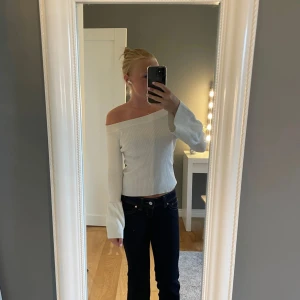 Vit offshoulder ribbad tröja - Säljer en vit ribbad tröja med offshoulder-modell och långa ärmar. Tröjan har en snygg, figurnära passform och vida ärmslut som ger en trendig look. Perfekt att styla med jeans eller kjol för en clean och fräsch vibe.