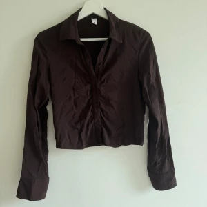 Brun skjorta från C.W. i bomull - Snygg brun skjorta från Carin Wester. i storlek 34. Modellen är croppad med klassisk krage och långa ärmar. Skjortan har knappar framtill och vid ärmsluten. Materialet är mjuk, perfekt för en chill och stilren look.