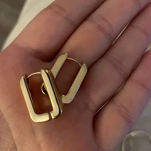 Guldiga chunky örhängen i fyrkantig form - Säljer ett par coola chunky örhängen i guld med fyrkantig, modern design. De är stilrena och har en slät yta som ger en lyxig känsla. Perfekta för dig som gillar statement-smycken och vill sticka ut lite extra.
