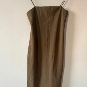 Khaki klänning H&M - Snygg grön klänning från H&M med smala axelband och rak, figurnära passform. Klänningen har en enkel, minimalistisk design som ger en cool vibe. Perfekt för dig som gillar stilrena plagg med en modern touch.