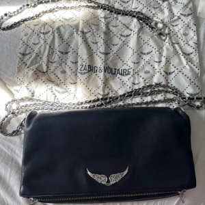 Svart axelväska från Zadig & Voltaire - Snygg svart axelväska i skinn från Zadig & Voltaire med silverfärgad kedja och dragkedja. Perfekt storlek för det viktigaste och kommer med dustbag och tags. Mycket bra skick