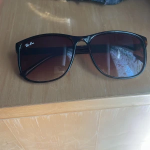 Bruna Ray-Ban solglasögon - Snygga svarta Ray-Ban solglasögon med klassisk pilotform och mörktonade linser. Ramen är i plast och har en stilren look som passar till många outfits. Perfekt för dig som vill ha en ikonisk accessoar med cool vibe. Aldrig används.