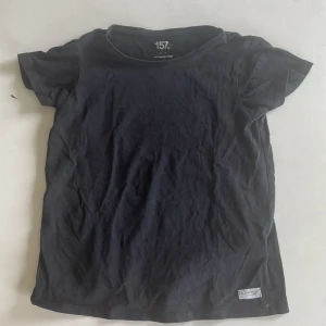 Svart t-shirt från 157, storlek 140 - En enkel svart t-shirt från 157 i storlek XS. Modellen är klassisk med rund hals och korta ärmar. Materialet är mjuk bomull med lite elastan för extra stretch och skön passform. Perfekt till jeans eller shorts, och funkar året runt.