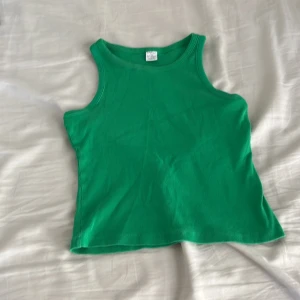 Grön ribbad linnetopp från Lindex - Snygg grön linnetopp från Lindex i ribbad bomull. Modellen är ärmlös med klassisk rund halsringning och croppad passform. Perfekt att matcha med jeans eller shorts för en chill look. Storlek 158/164, passar dig som gillar enkel och färgstark stil.