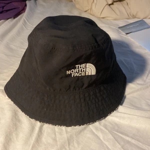 Svart bucket hat från The North Face - Snygg svart bucket hat från The North Face med broderad vit logga framtill. Hatten har klassisk rund form och bred brätte, perfekt för att ge skön streetstil. Tillverkad i lätt polyester som andas och är bekväm att bära hela dagen.
