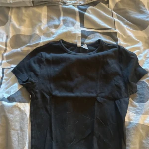 Svart ribbad t-shirt från H&M Divided - Svart t-shirt från H&M Divided i ribbad bomull. Modellen är klassisk med rund hals och korta ärmar, perfekt för en chill och enkel stil. Passformen är normal och materialet är mjukt och skönt mot huden.