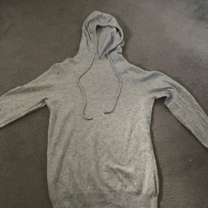Kashmir hoodie - Mjuk och enkel grå hoodie med huva och snörning. Tröjan har långa ärmar och ribbade muddar vid ärmslut och nederkant. Perfekt för chill dagar och passar till allt. Materialet känns skönt mot huden och har en klassisk loose passform. Storlek S passar även xs.