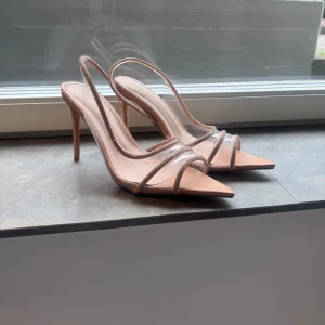 Beiga klackpumps med transparenta band - Snygga pumps i beige med spetsig tå och hög klack. Skorna har transparenta band med glittriga detaljer och öppen häl.  Skorna är endast använda en gång men ser lite dammiga ut på bilden då de stått oanvända ett tag men tvättas bort med lite vattnen bara 