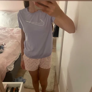 Ljuslila Nike t-shirt med logga - Säljer en ljuslila t-shirt från Nike med stor vit swoosh-logga på bröstet. T-shirten har rund hals, korta ärmar och är gjord i mjukt, lätt polyester. Träningsmaterial och perfekt för alla sporter, alltifrån gym till fotboll. Storlek 146-152