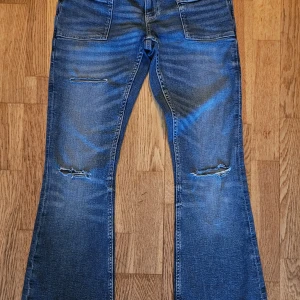 14+ pleated flare jeans - Säljer ett par blå jeans från Gina Tricot med bootcut passform och snygga slitningar på knäna. Jeansen har framfickor med markerade sömmar och klassiska bakfickor. Perfekt för dig som gillar en avslappnad och trendig stil. Materialet är jeans med en skön känsla. Knappt använda. Strl M i Ginas +14 så lite svårt att uppskatta storlek 