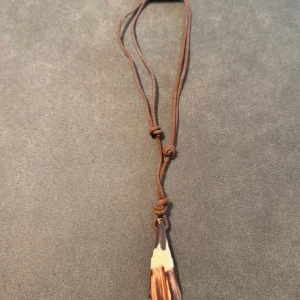 Brunt halsband med hornformad hänge - Unikt halsband med justerbart brunt snöre och ett hornformad hänge i naturfärger. Hänget har en mix av bruna och beige toner med naturliga mönster, vilket ger en cool och jordnära vibe. Perfekt för dig som gillar boho eller naturinspirerad stil. Står ej för frakt 