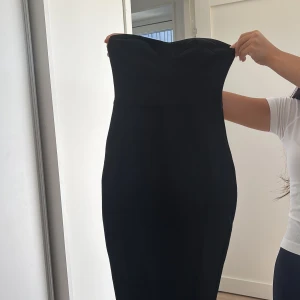 Svart axelbandslös långklänning - Säljer en svart axelbandslös långklänning med figurnära passform och snygg slits bak. Klänningen har en markerad byst och dragkedja i ryggen för enkel påklädning. Materialet är stretchigt och ger en smickrande siluett. Perfekt för dig som vill ha en elegant look. Priset kan diskuteras💞