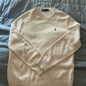 Beige stickad tröja från Polo Ralph Lauren - Säljer en beige stickad tröja från Polo Ralph Lauren i storlek L. Tröjan har rund hals, ribbade muddar och det klassiska blå Polo-logot på bröstet. Perfekt för dig som gillar stilrena och tidlösa plagg med premiumkänsla.