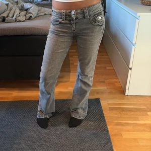 Grå bootcut jeans med låg midja - Säljer ett par grå jeans med snygg bootcut och låg midja. Jeansen har klassiska fem fickor, dubbla knappar i midjan och coola detaljer på framfickorna. Perfekt passform för dig som gillar en avslappnad men trendig look.