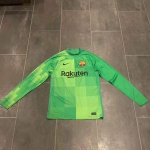 Barcelona målvaktströja Ter Stegen S - Säljer en grön långärmad FC Barcelona målvaktströja från Nike med Ter Stegen och nummer 1 på ryggen. Tröjan har pixelmönster på ärmarna, klubbmärke och Rakuten-logga på bröstet samt Dri-Fit-material som andas. Perfekt för dig som vill sticka ut på planen.