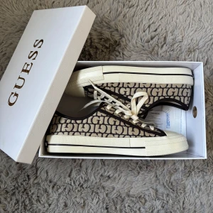 Beige och bruna sneakers från Guess - Snygga sneakers från Guess med beige och brunt monogrammönster. Säljer då dom är för stora för mig💞