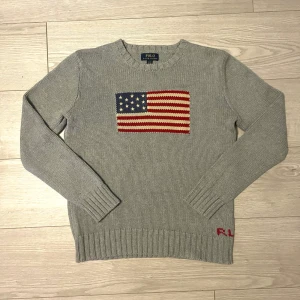 Grå stickad tröja Polo Ralph Lauren 🇺🇸💯 - 💯Snygg grå stickad tröja från Polo Ralph Lauren med amerikansk flagga broderad på bröstet och RL-broderi vid nederkanten.💯 ✅Tröjan har rund hals och långa ärmar med ribbade muddar.✅Storlek 18-20 men sitter som M.