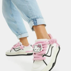 Hello Kitty sneakers med fluffiga rosa snören - Unika sneakers i vitt med svarta detaljer och fluffiga rosa snören, prydda med en stor Hello Kitty-dekoration på varje sko. Insidan är rosa och sulan är platt med svart kant. Perfekt för dig som vill sticka ut med en söt och lekfull stil. Säljer pågrund av storlek och jag köpte den utomlands så hann inte testa den så bra. 