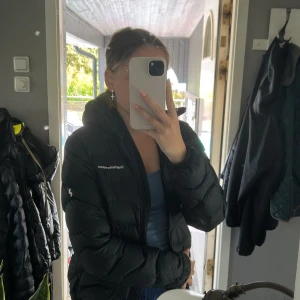 Svart dunjacka från Peak Performance - Säljer en svart dunjacka från Peak Performance med huva och dragkedja framtill. Jackan har en puffad look och loggan broderad på bröstet. Perfekt för kyliga dagar och riktigt snygg till jeans eller mjukis. Fråga gärna om du vill veta mer!