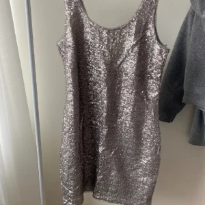 Glittrig silverklänning Gina Tricot - Säljer en snygg glittrig silverklänning från Gina Tricot i storlek M. Klänningen är kort, ärmlös och har en rundad halsringning. Perfekt för dig som vill sticka ut med paljetter och metallic-look. Materialet är polyester med paljettöverdrag.