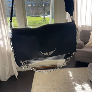 Zadig & Voltaire - axelremsväska  - Höjd: 22 cm i storlek, Längd: 30 cm i storlek, Vidd: 6cm i storlek, Handtag: 34 cm i storlek. Väskan är av skinn med en prydnadskedja, har magnetlås och är rymlig (perfekt till vardag!). Insidan är av textil. Säljer väskan då jag köpt en annan modell