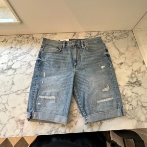 Nya ljusblå rivna jeansshorts  - Ett par helt nya riva mörkblå jeansshorts. Shortsen är tunga men mjuka och sitter perfekt på kroppen. De har passformen slim fit och är tillräckligt luftiga för att spendera en hel sommar i de. Fick de i present av en släkting. 