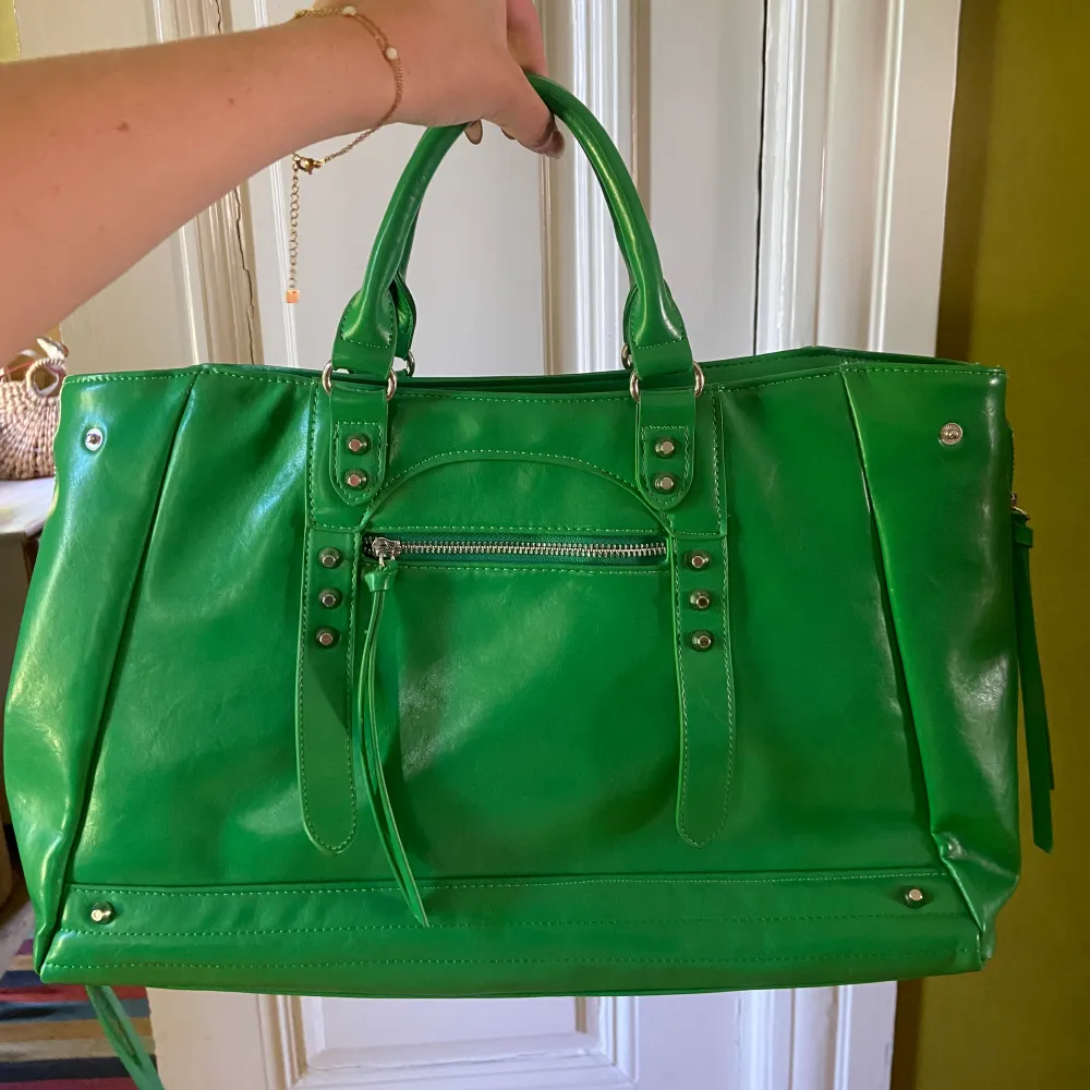 Handväska från Nakd som rymmer mycket. Den är grön med silvriga detaljer, väskan är i nyskick. Medföljer axelrem! . Väskor.