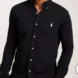Polo Ralph Lauren skjorta - Jättesnygg svart skjorta med vita knappar (slim fit) i fint skick, otroligt snygg till ljusa linnebyxor, men som tyvärr är för liten.