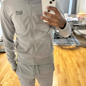 Exklusiv Grå träningsoverall från Emporio Armani EA7 - Uppgradera din garderob med denna stilrena grå  från Emporio Armani EA7. Designad med dragkedja, praktiska fickor och en perfekt 