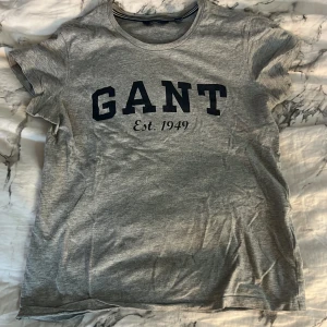 GANT t-shirt - Den är använd men fortfarande i bra skick. Den är i färjen grå med marinblå text.