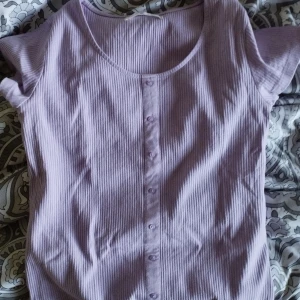 Lila topp - Ribbad, med knappar och lite kort i modellen. 