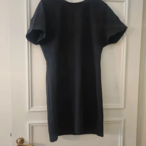 Svart klänning - En elegant svart klänning med korta ärmar och en knytning i midjan. Klänningen har en enkel och stilren design, perfekt för både formella och semi-formella tillfällen.