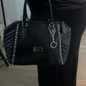 Jättesnygg svart väska från Guess! Köpt på Sellpy därav äkthetskontrollerad💓 Bredd: 30cm, djup: 19cm, höjd: 22cm. Väskan har  defekter. (Skriv för fler bilder)