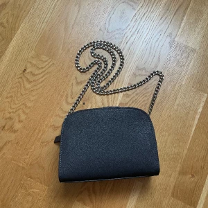 Liten festig väska  - Grå/brun liten väska från H&M med kedja som axelremsband. Aldrig använd! Bakgrunden på sista bilden är svart. 